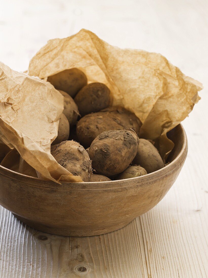 Fresh potatoes in torn paper bag in bowl