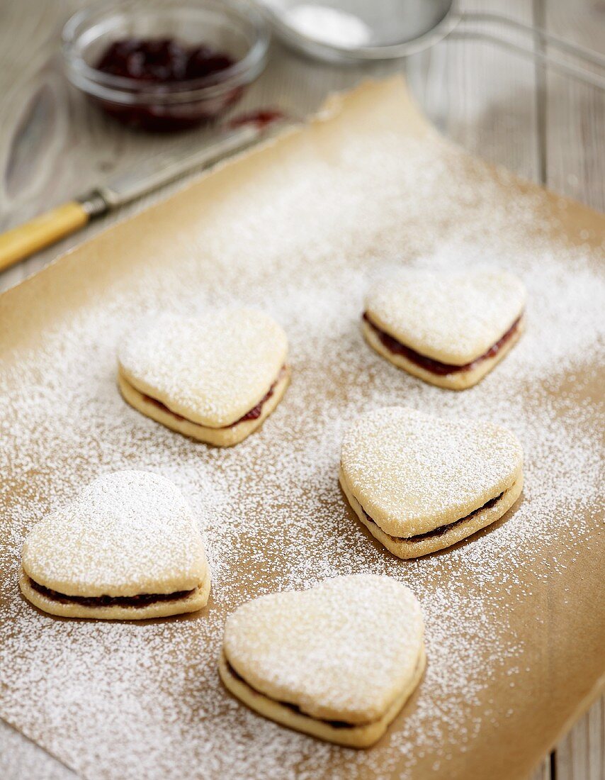 Heart-shaped jam sandwich biscuits on baking parchment