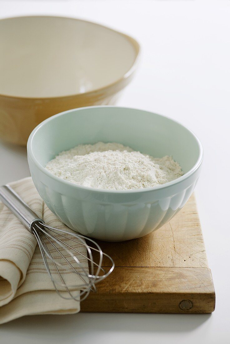 Flour in bowl, whisk and cloth on chopping board