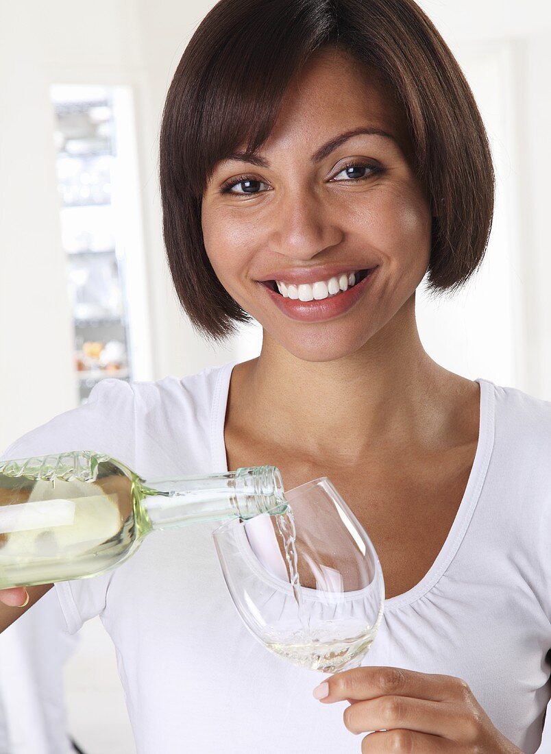 A woman pouring white wine from a bottle into a glass