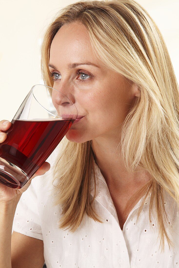 A blonde woman drinking a glass of red juice