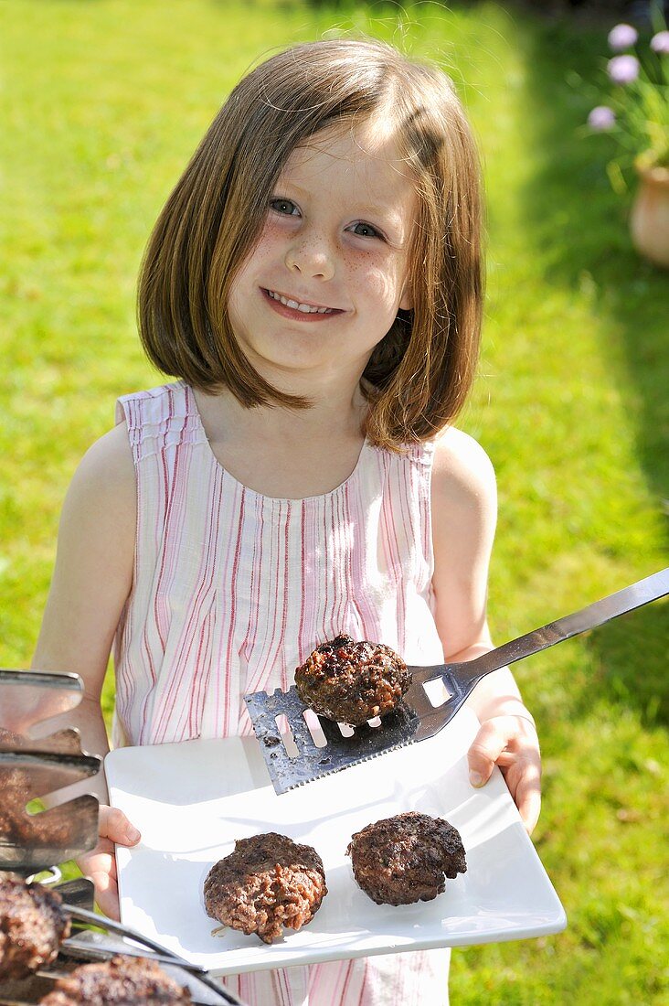 A girl holding a plate of grilled meatballs