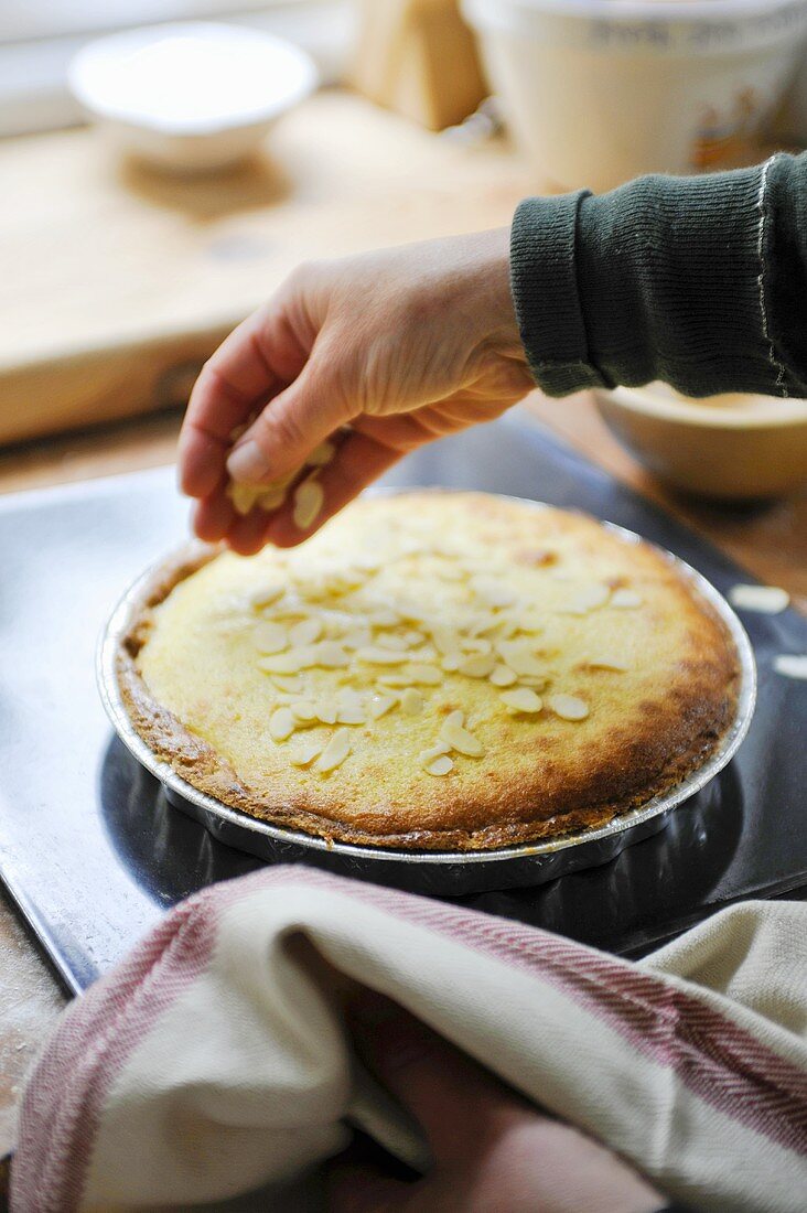 A hand sprinkling almonds on a Bakewell tart