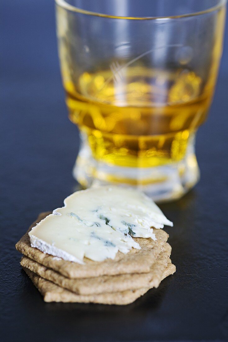 Blauschimmelkäse (Sorte: Mrs Temple's Binham Blue, Norfolk, UK) auf Crackern vor Whiskeyglas