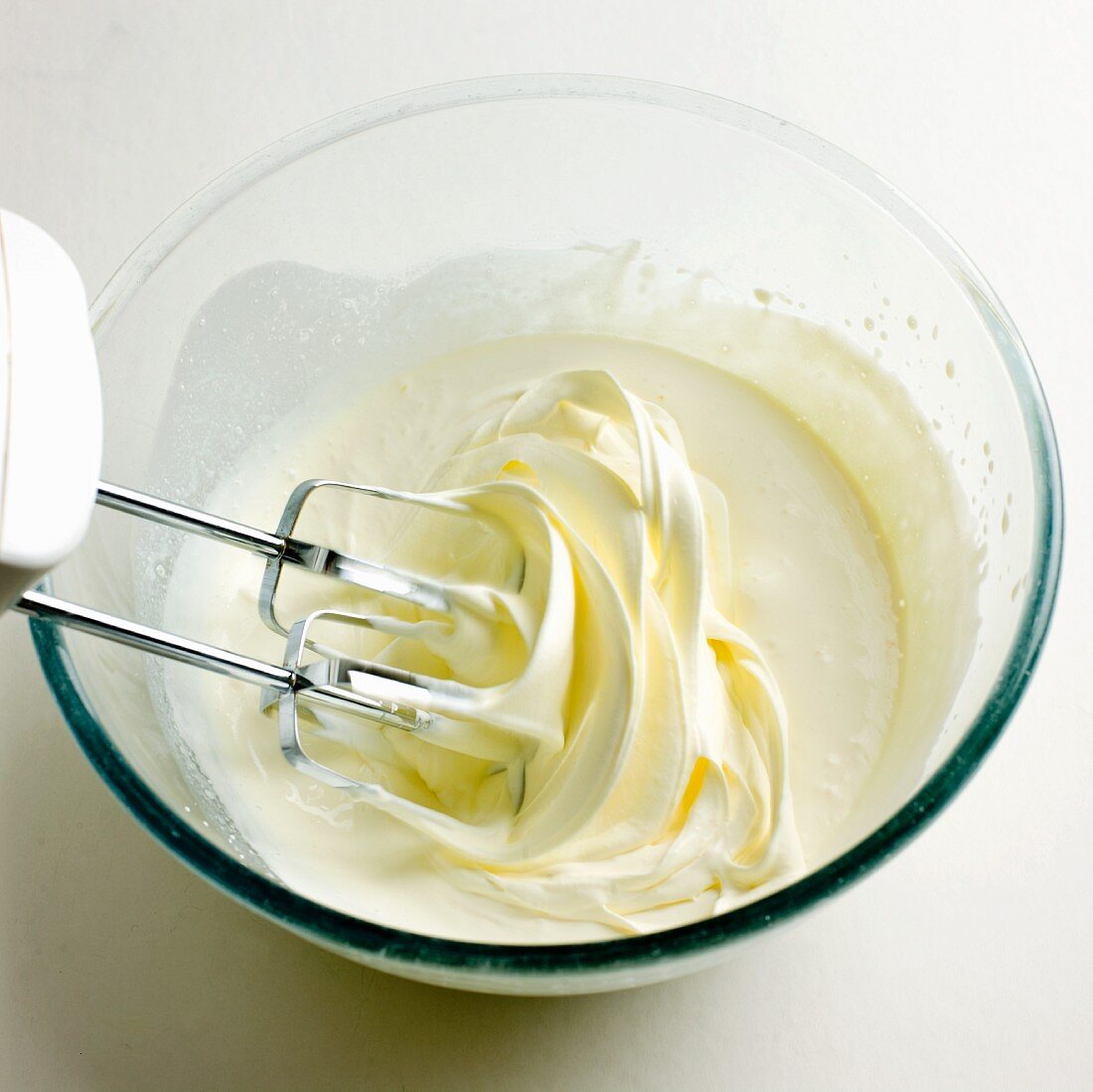 Cream being whipped in a glass bowl with an electric whisk