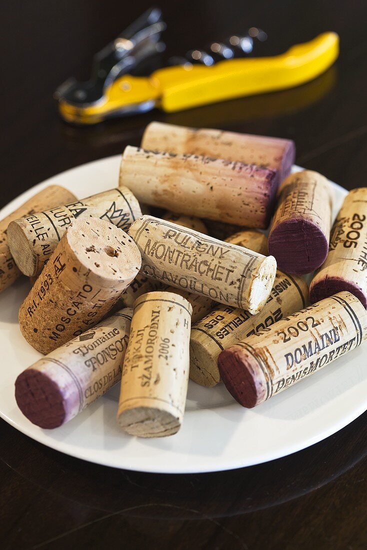 Various wine corks on a plate with a cork screw in the background