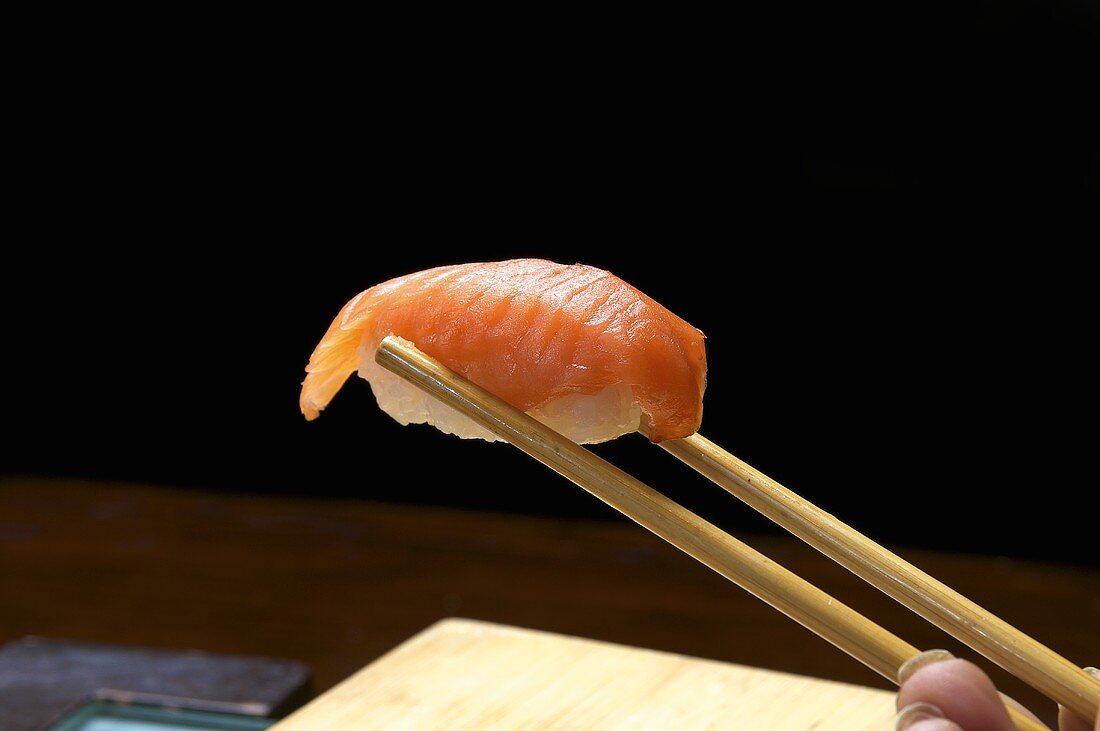 A hand holding a nigiri sushi in chopsticks