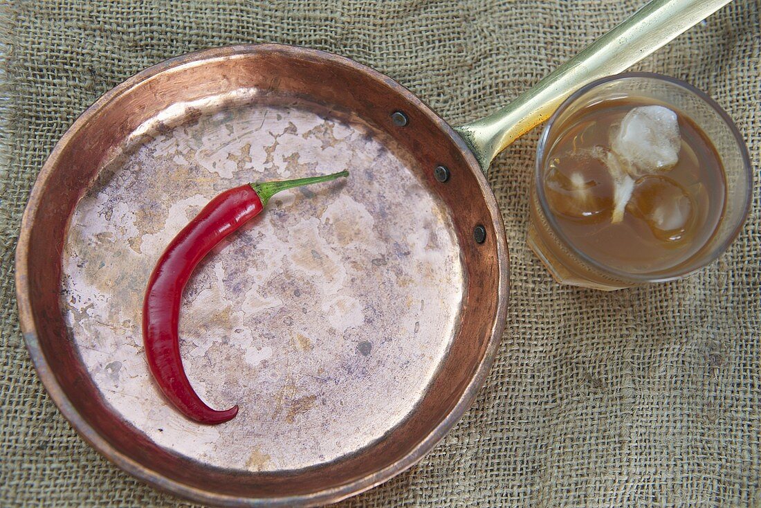 A red chilli pepper in a pan with a glass of palm fruit juice