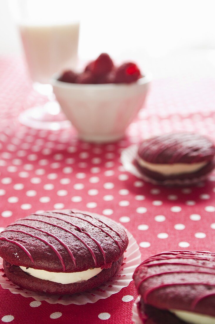 Himbeer-Whoopie Pies auf gepunktetem Tischtuch, frische Himbeeren, Milchglas