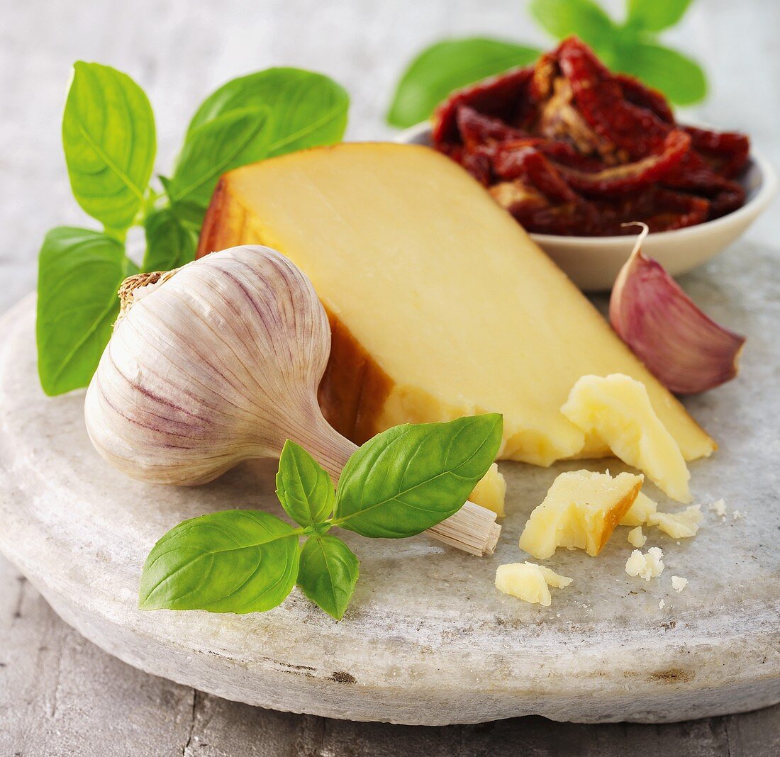 Ein Stück Räucherkäse daneben Knoblauch & getrocknete Tomaten