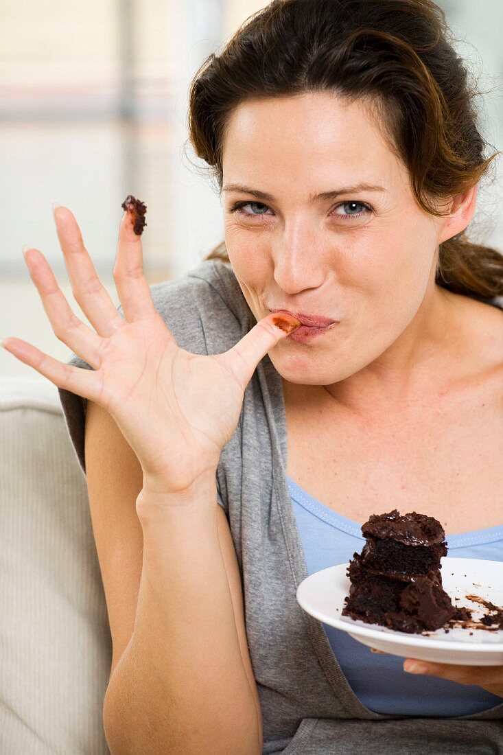 Frau nascht Schokoladenkuchen auf dem Sofa