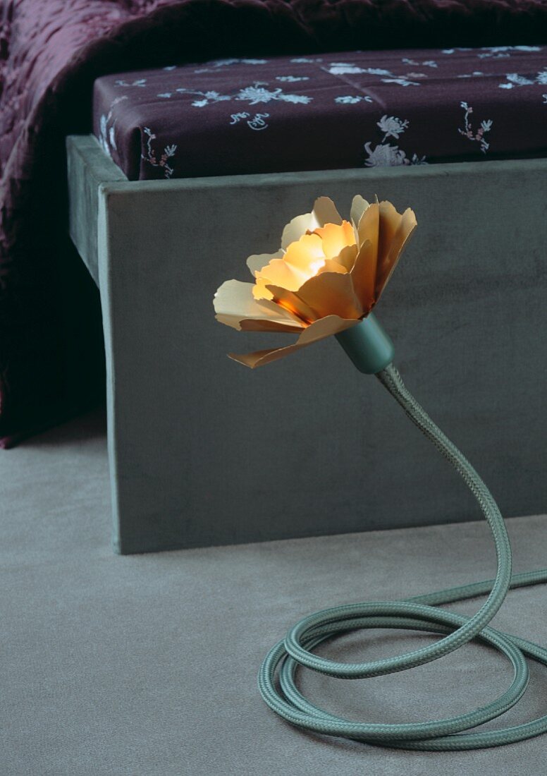 Flower-shaped table lamp with adjustable base at foot of bed