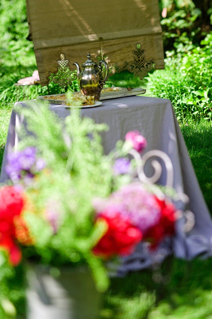 Blumenstrauss, dahinter Tisch mit Silberkanne und Kuchen