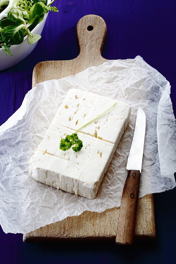 Feta cheese and a knife on a slice of paper on a wooden board