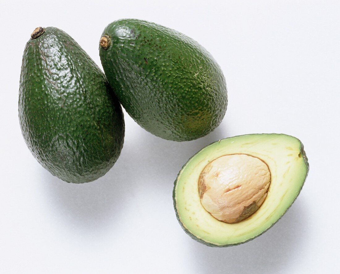 Two whole avocados and half an avocado with stone