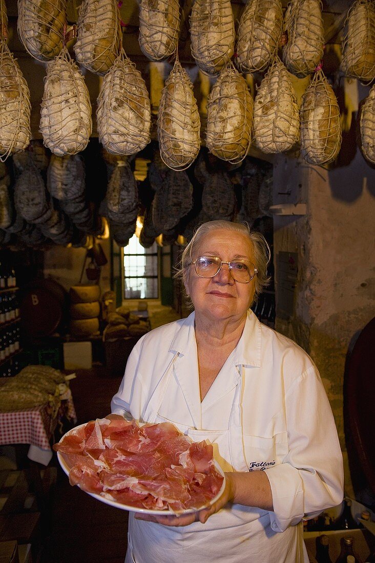 A woman carrying a plate of sliced culatello