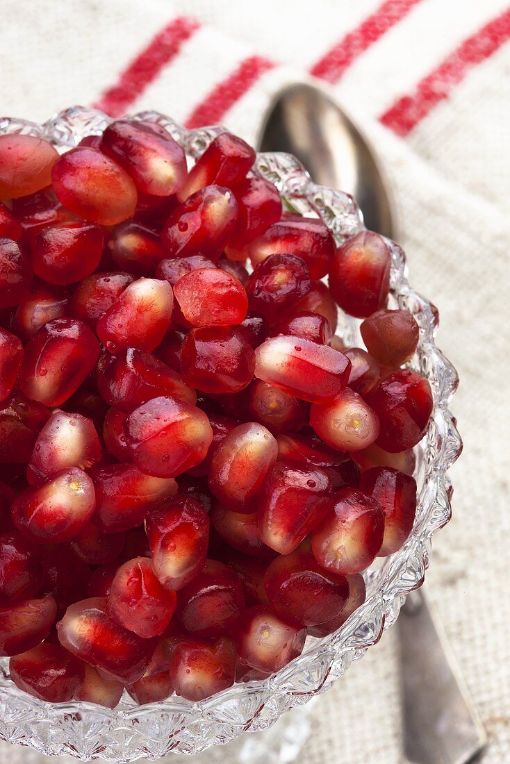 Pomegranate seeds in a glass bowl with a spoon