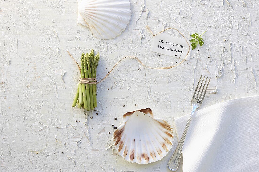 A bunch of asparagus, scallops, a napkin and a fork