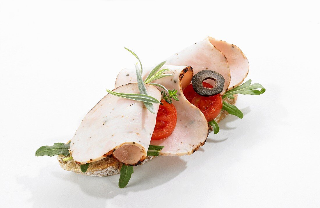 An open sandwich topped with turkey, rocket, tomatoes and olives