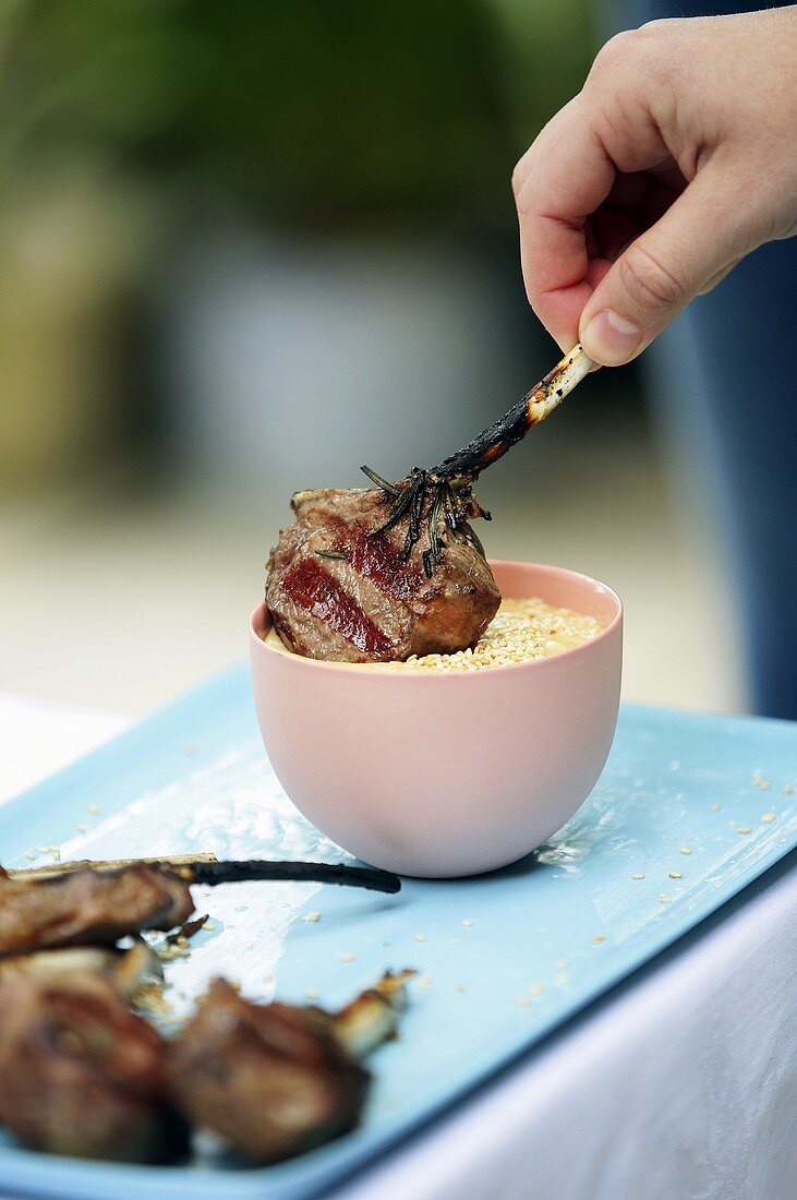 A hand dipping a lamb chop into sesame paste