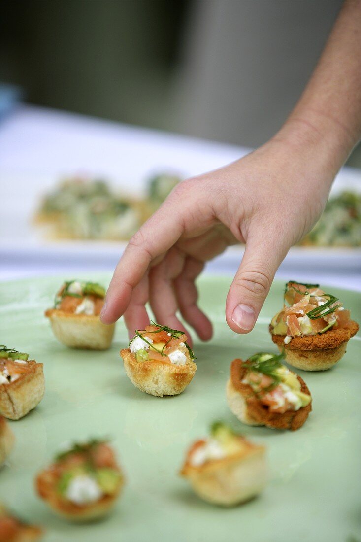 A hand reaching for a salmon and avocado tartlet