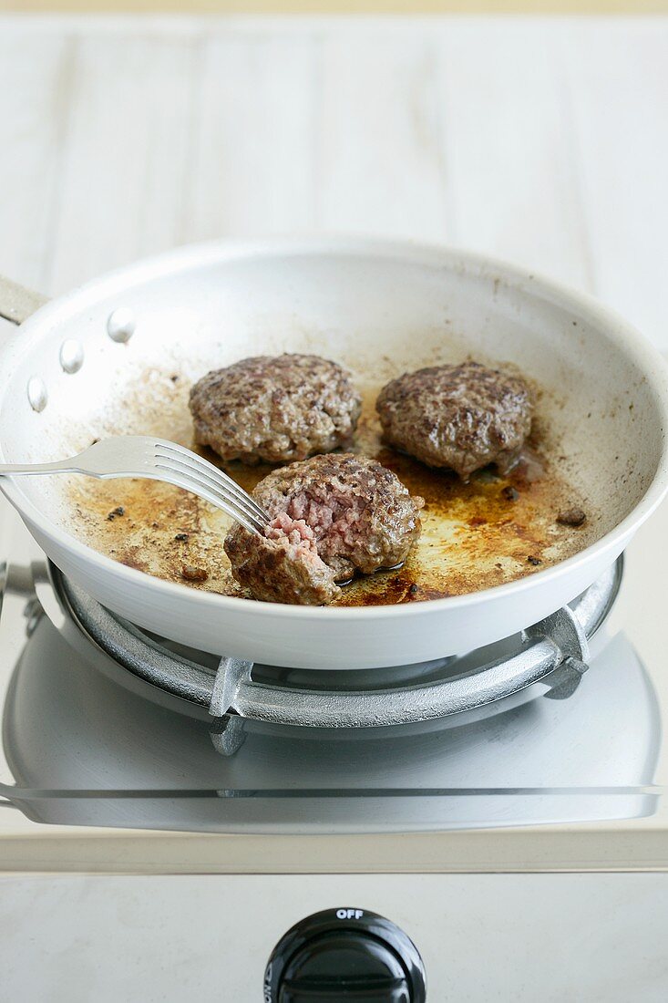 Burgers being fried in a pan