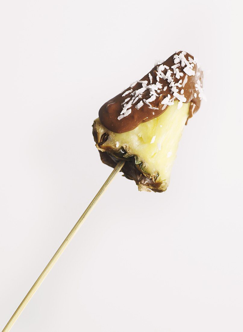 A piece of pineapple with chocolate and coconut on a kebab stick