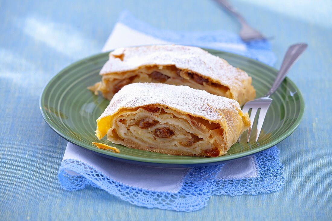 Two slices of apple strudel with hazelnuts, raisins and icing sugar