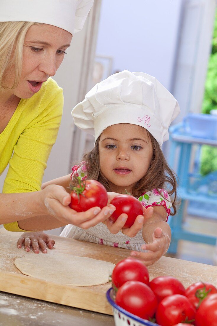 A mother and daughter with tomatoes and pizza dough