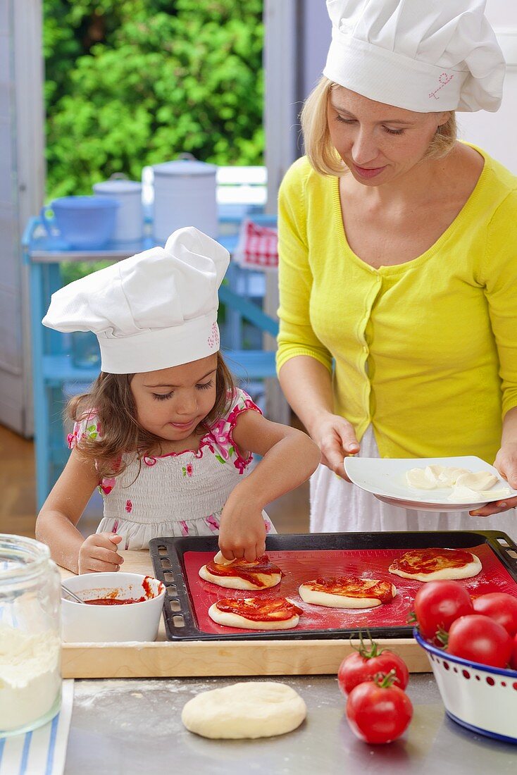 A mother and daughter placing toppings on a pizza