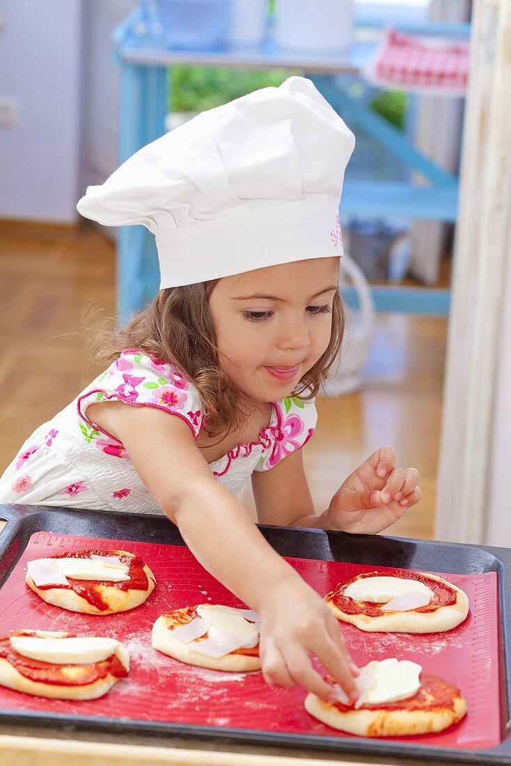 A little girl placing toppings on a pizza