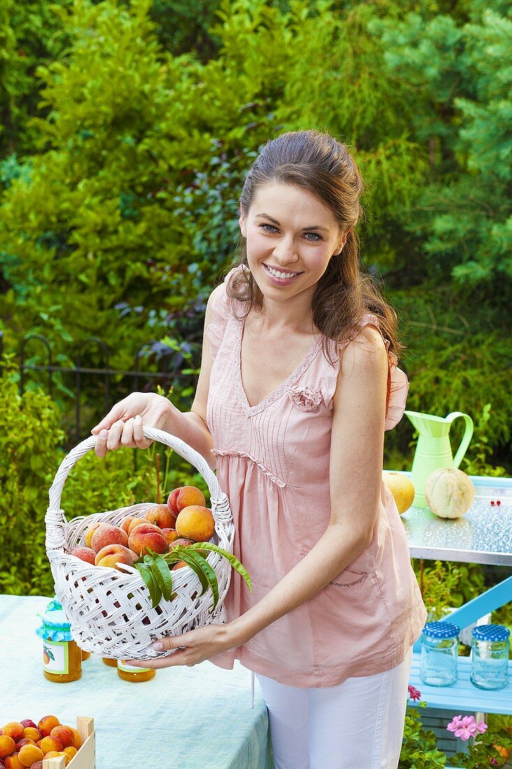 Junge Frau zeigt einen Korb mit frischen Pfirsichen