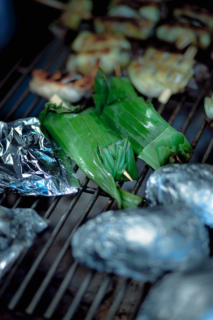 Halibut wrapped in banana leaves, potatoes in aluminum foil and eggplant rolls on the grill
