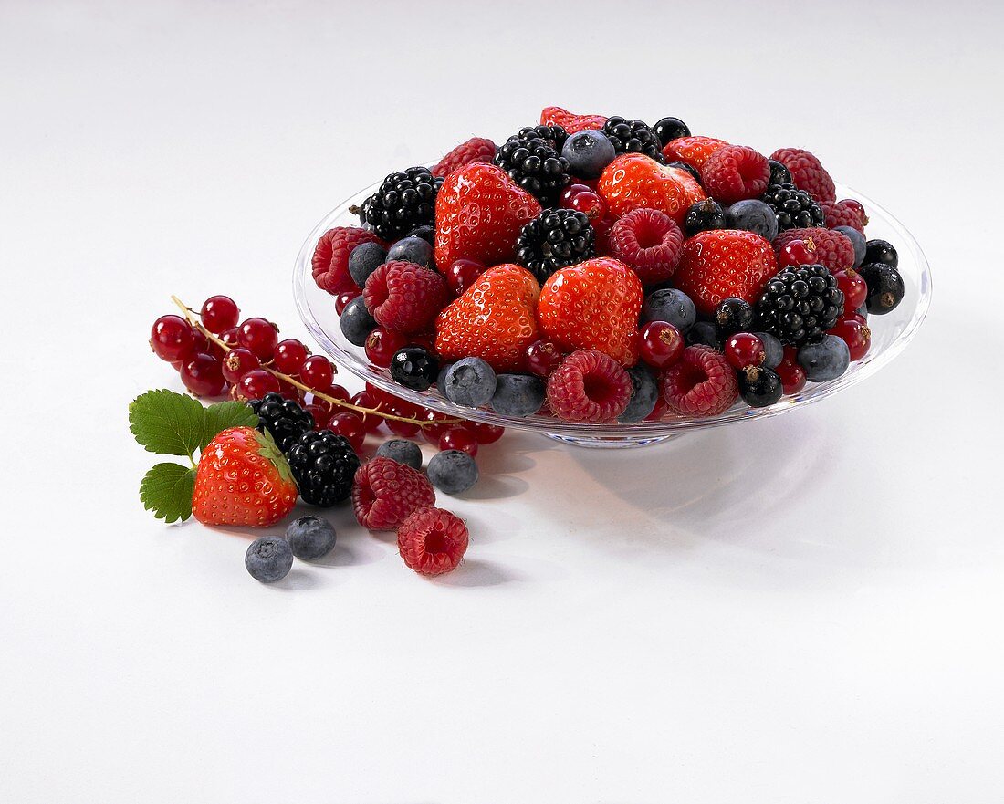 Assorted berries in a glass dish with more berries next to it
