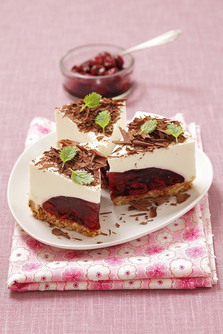 Drei Stücke Käsekuchen mit Kirschgelee und Schokospänen