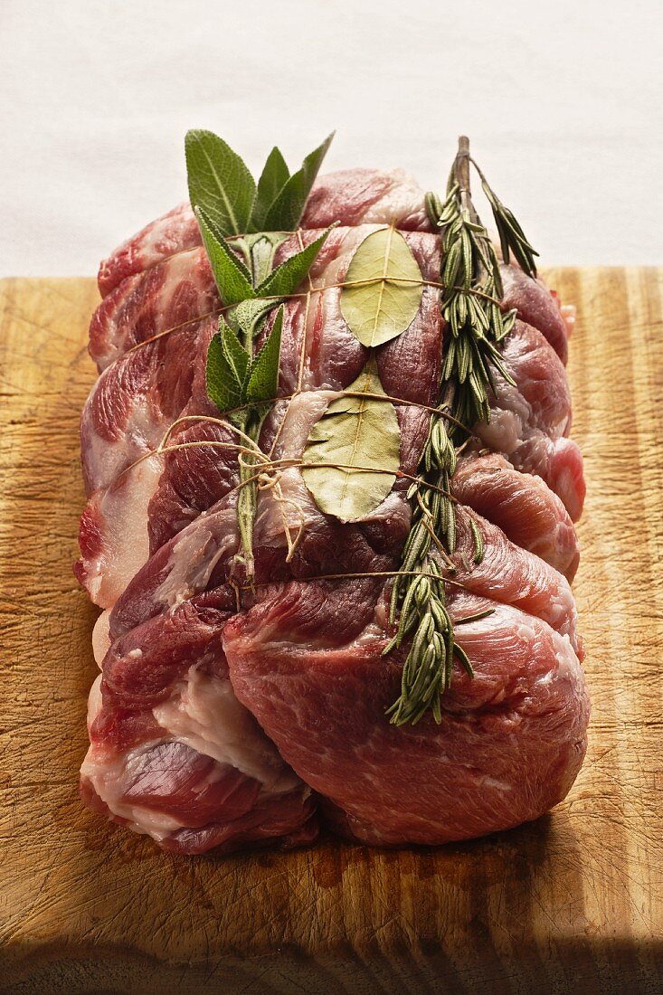Raw rolled roast pork with rosemary, bay leaf and sage