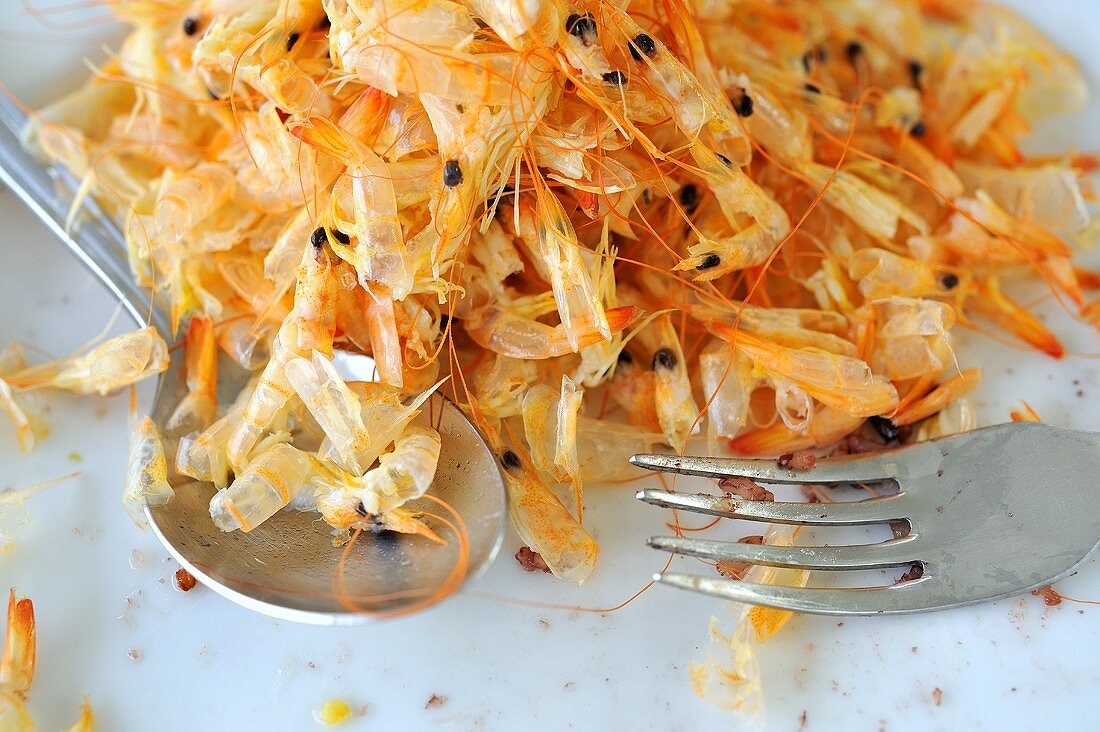 A pile of prawn shells with a fork and a spoon