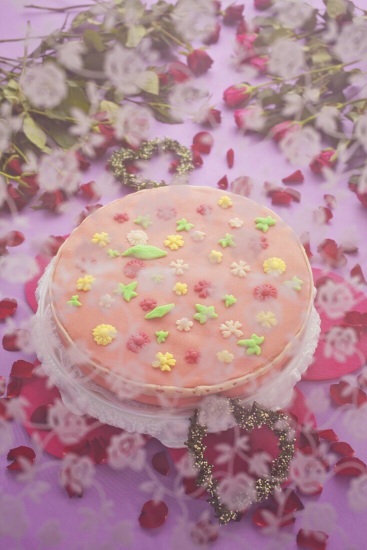 A cake with pink sugar icing and flowers underneath a veil