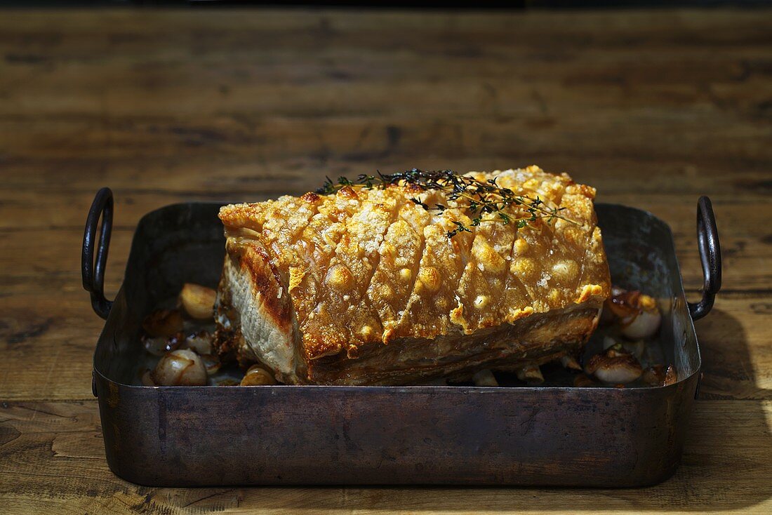 Roast pork in a roasting tin on a rustic wooden table