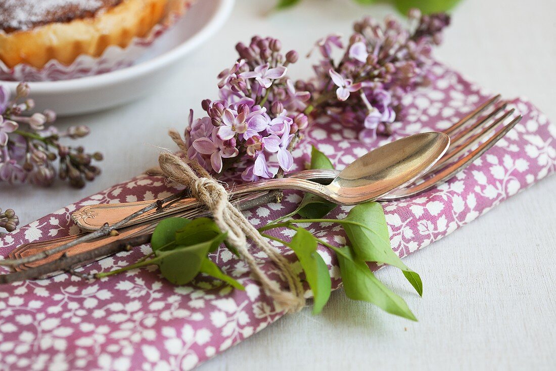 A napkin, cutlery and lilac tied together