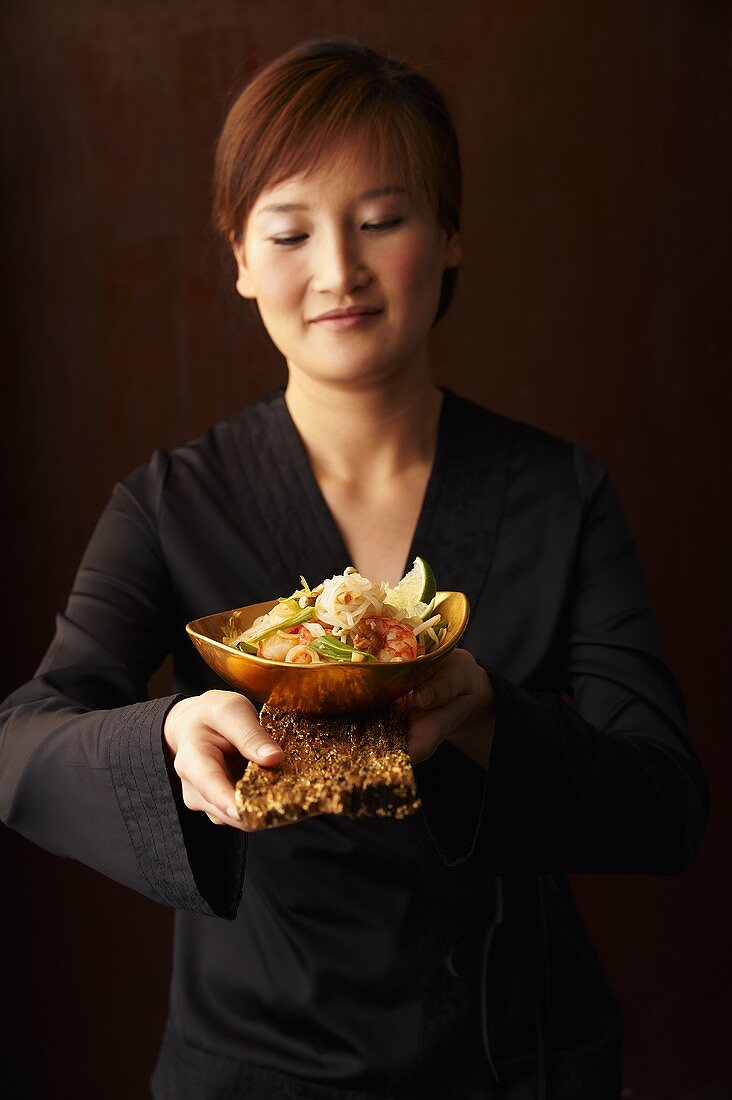 A woman holding a bowl of pad thai (fried rice noodles, Thailand)
