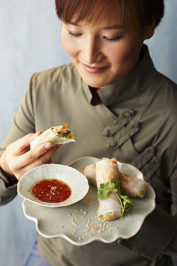 A woman eating spring rolls with nuoc cham dip (chilli fish sauce, Vietnam)