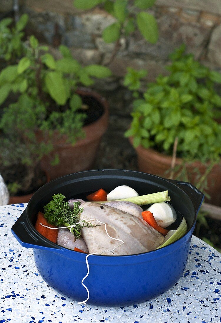 A raw chicken in a pot with ingredients for poaching