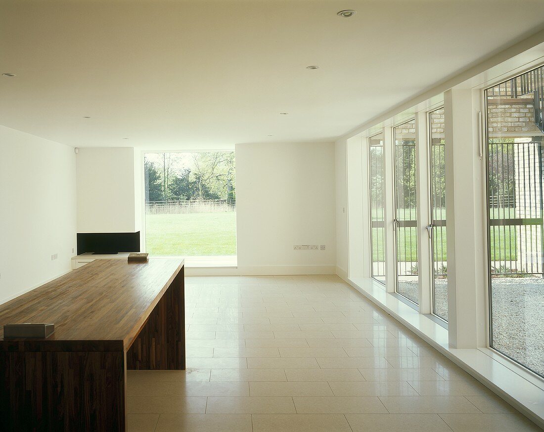 A modern living room with wooden designer table and floor-to-ceiling windows with a view of the garden