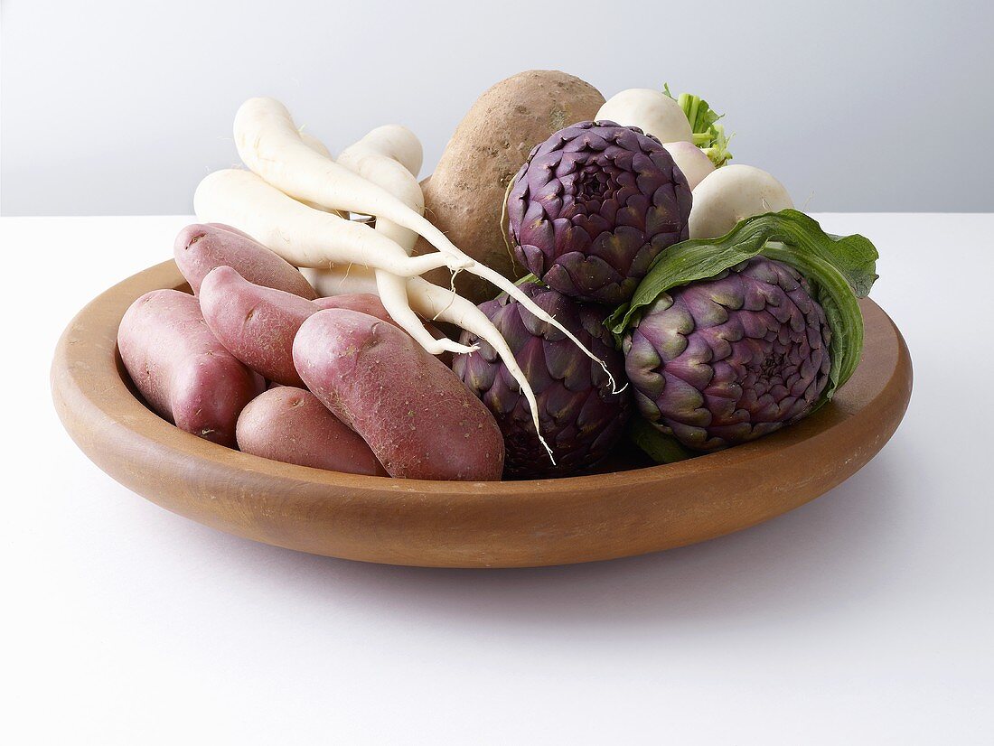 Potatoes, artichokes, radish and carrots on a wooden plate
