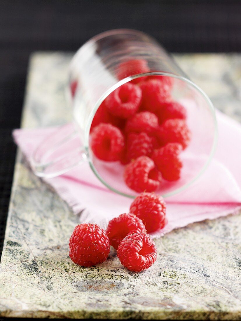 Fresh raspberries spilling out of a glass