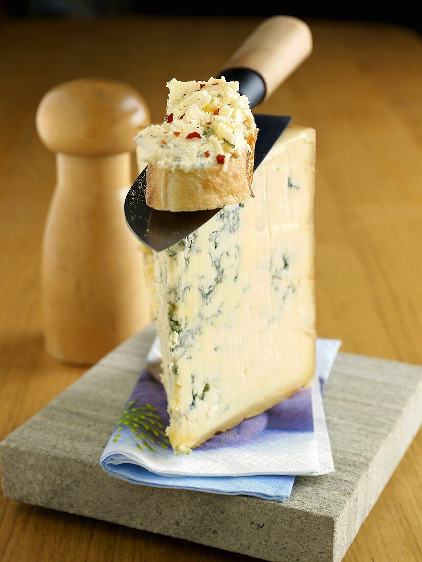A slice of Stilton with a knife and cheese bread