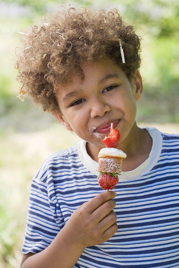 A little boy eating a strawberry muffin kebab