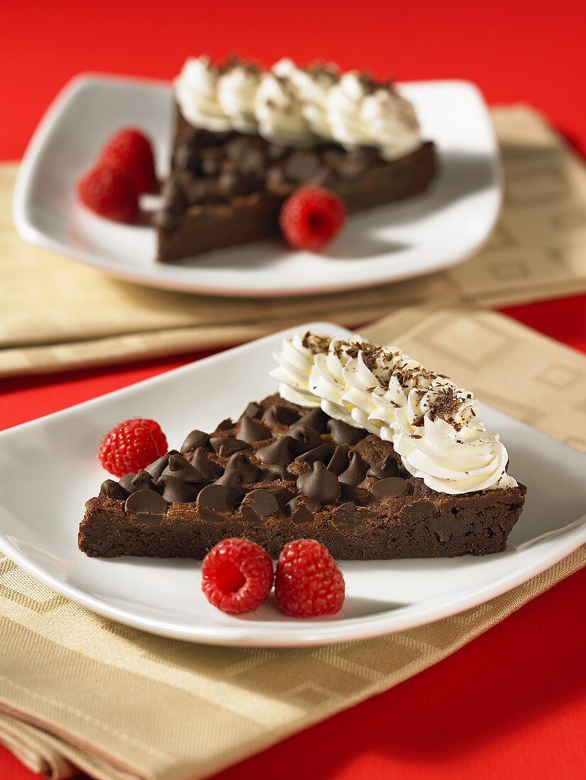 Two slices of chocolate chip brownie tart with whipped cream and raspberries