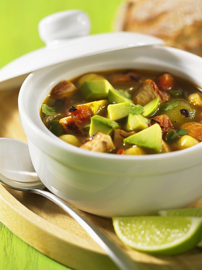 Chicken soup with avocado in a pot with lime wedges